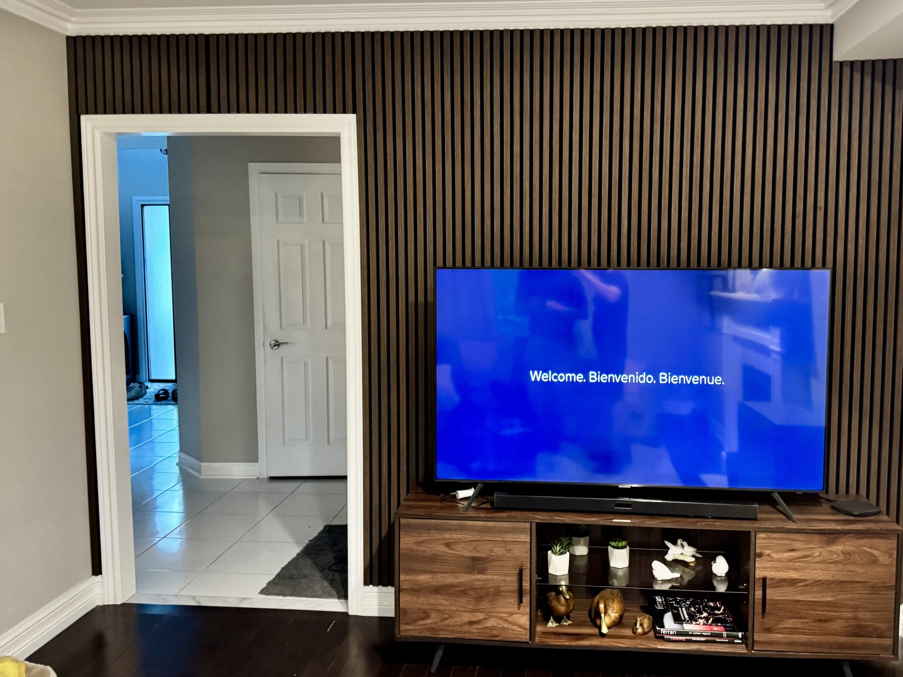 The finished living room: a full-height walnut slat wall running behind the television and wrapping past the doorway.