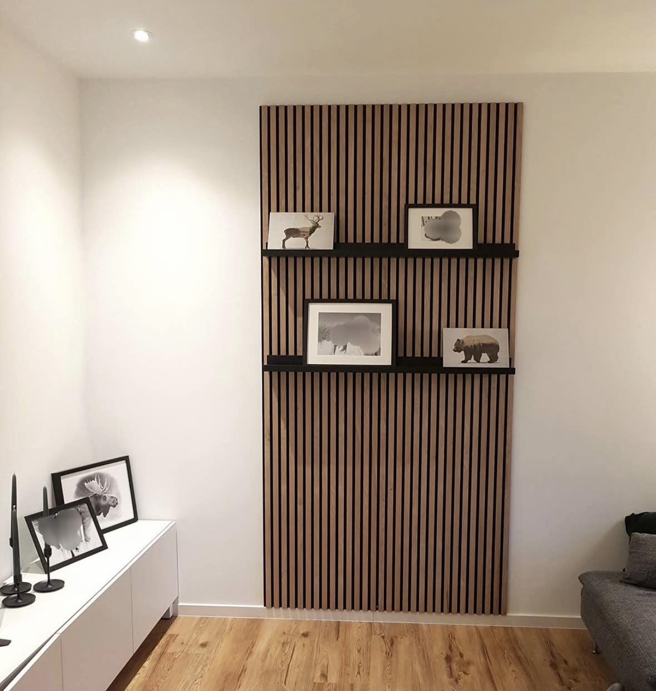Oak slat wall fitted with black picture ledges holding framed prints.
