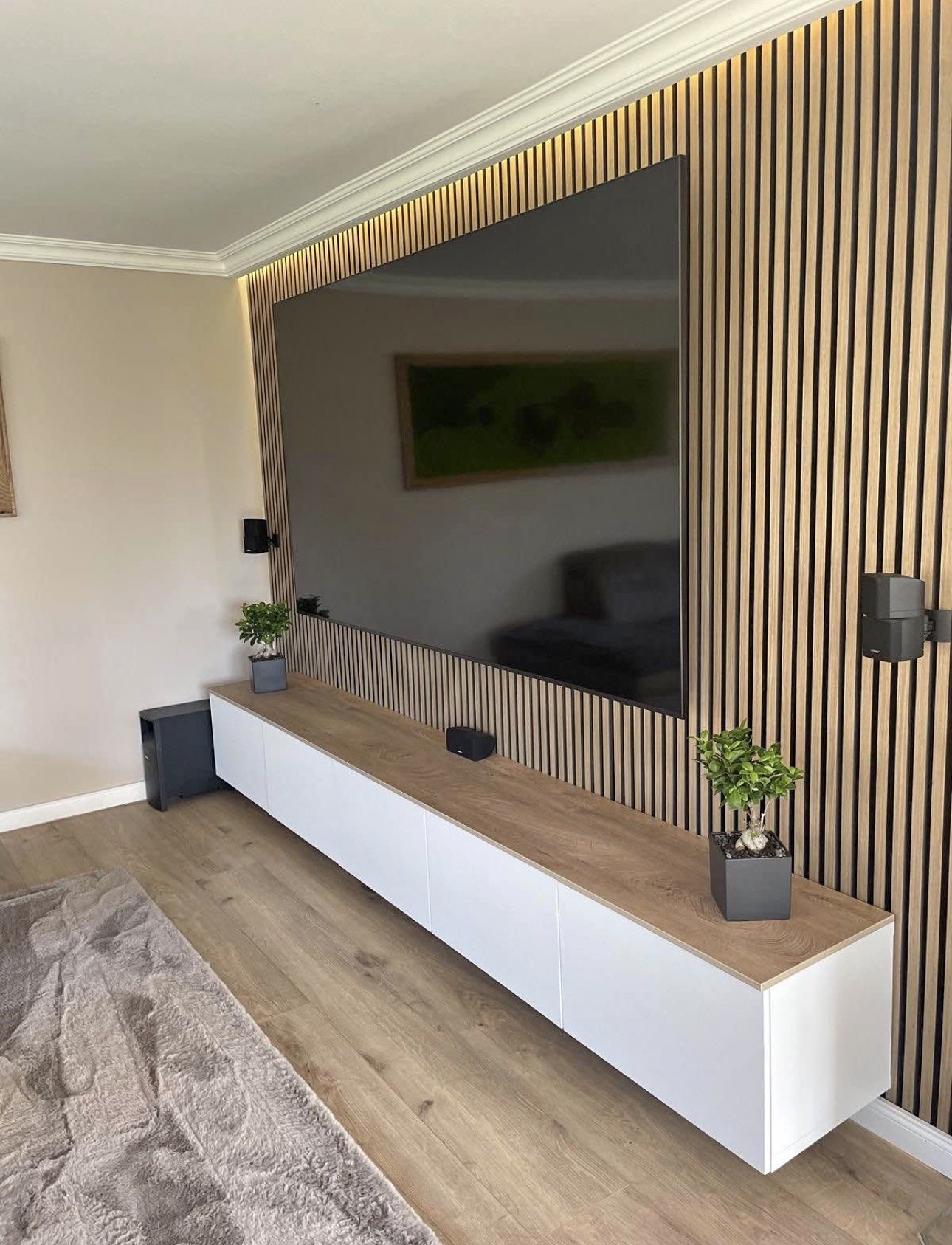 Warm oak slat wall with a long floating white console and LED cove lighting along the ceiling.